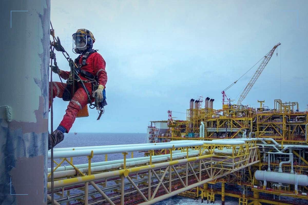 Technician in protective gear working on rope beside industrial pipework