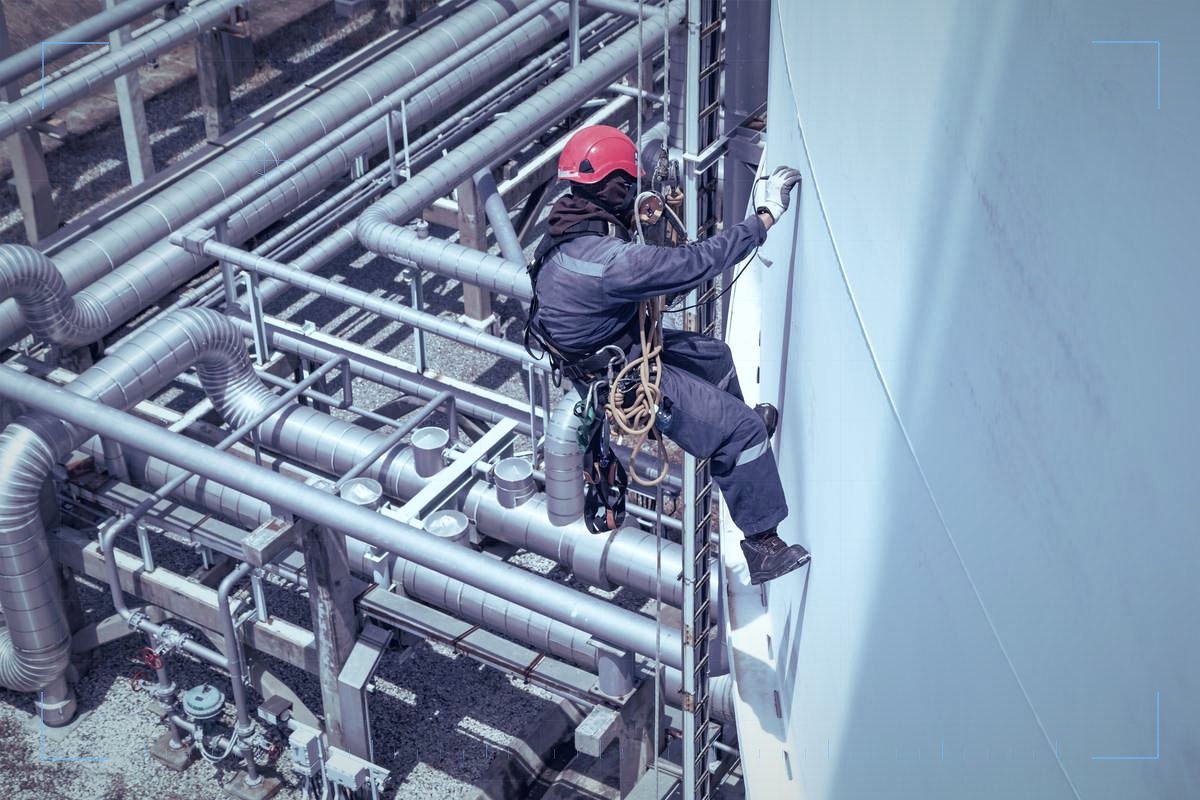 Rope access technician in a red helmet working on a pipework and tank structure
